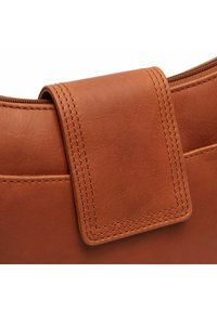 Bolso de cuero marrón con una textura suave y un cierre de solapa cosido destacado. El diseño presenta bordes curvados sutiles y una parte superior con cremallera.