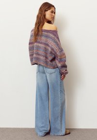 Oversized, multi-colored knit sweater with off-shoulder design, paired with wide-leg light blue denim jeans. Soft texture, casual fit.