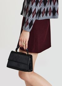 Sac à main en simili cuir noir avec une silhouette structurée, une poignée supérieure et une fermeture à fermoir. Présente des coutures minimales et aucun accent matériel visible.