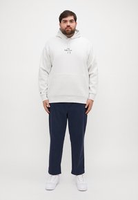 Απαλή γκρίζα ζακέτα με τσέπη μπροστά και κουκούλα με κορδόνια, συνδυασμένη με ναυτικά παντελόνια και λευκά αθλητικά παπούτσια. Απλός σχεδιασμός και άνετη εφαρμογή.