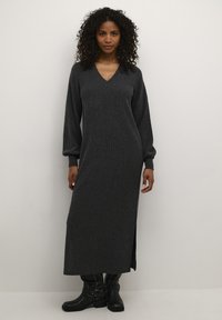 Robe longue gris foncé avec un décolleté en V, texture côtelée et manches ballon ; présente une fente latérale et est associée à des bottines noires.
