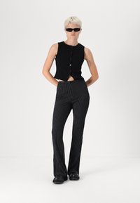 Μαύρη δομημένη αμάνικη μπλούζα με κουμπιά μπροστά, σε συνδυασμό με μαύρες και λευκές ριγωτές φούστες σε φαρδιά γραμμή και χοντρά μαύρα παπούτσια.