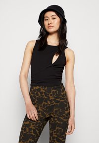 Top preto sem mangas com detalhe recortado, tecido texturizado, combinado com calças de cintura alta de padrão leopardo castanho. Chapéu bucket preto sólido.