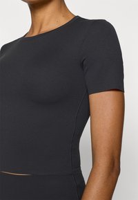 Μαύρο εφαρμοστό τοπ με κοντά μανίκια, κατασκευασμένο από λείο, ελαστικό ύφασμα· διαθέτει στρογγυλή λαιμόκοψη και διακριτικές ραφές στις πλευρές.