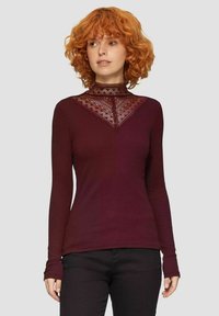 Bordeauxrode lange mouwen shirt met een hoge halslijn en kantdetails in een V-vorm. Geribbelde textuur en aansluitend ontwerp, gedragen met zwarte broek.