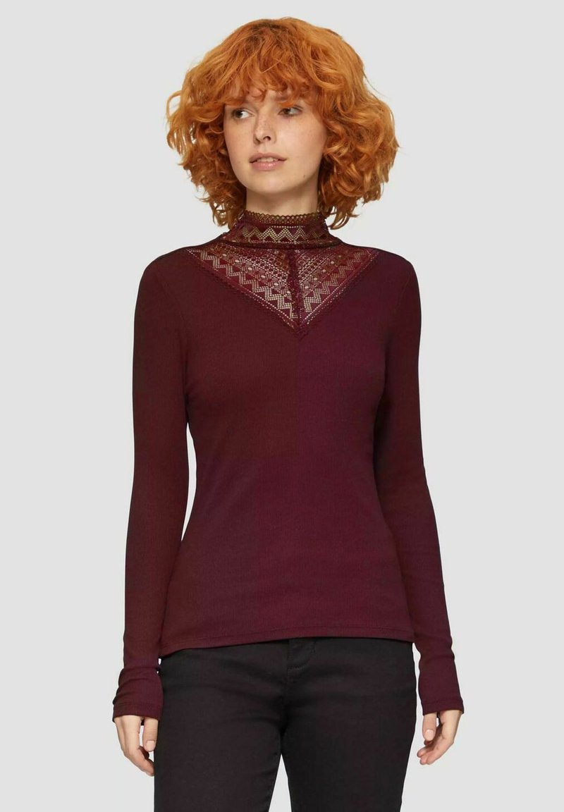 Bordeauxrode lange mouwen shirt met een hoge halslijn en kantdetails in een V-vorm. Geribbelde textuur en aansluitend ontwerp, gedragen met zwarte broek.