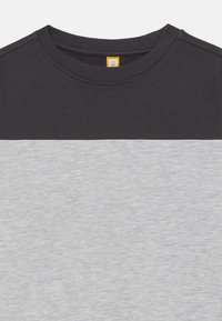 T-shirt en coton avec un col rond, présentant une section supérieure gris foncé et une section inférieure gris clair, texture lisse et couleurs contrastées.