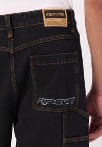 Sorte denim cargo bukser med kontrastorange syninger, der har en stor sidelomme og et lædermærke på livlinen.
