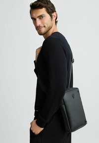 Borsa a spalla in pelle nera con un design rettangolare elegante, dotata di chiusura con zip e tracolla regolabile. Finitura texturizzata con dettagli del logo.