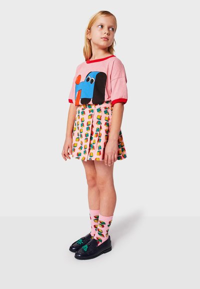 Camiseta corta de manga rosa con un gráfico de perro azul y negro, combinada con una falda plisada que presenta patrones de casas coloridas y calcetines rosas.
