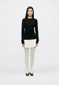 Pulover negru cu mâneci lungi, cu model rib, asortat cu o fustă mini plisată albă. Modelul poartă ciorapi albi transparenți și pantofi negri fără toc.