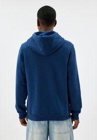 Sudadera azul marino hecha de tela suave, cuenta con una capucha con cordones, puños y dobladillo acanalados, con un diseño simple y sin logotipos.