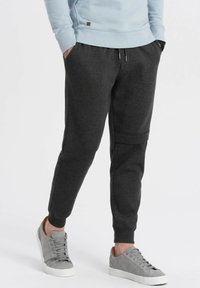 Donkergrijze joggerbroek gemaakt van zachte stof, met een taps toelopend ontwerp, een elastische tailleband en zijzakken, gedragen met grijze sneakers.