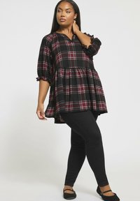 Tunic a quadri neri e rossi con maniche a sbuffo e polsini arricciati, abbinata a leggings neri slim-fit e ballerine nere. Stile verticale.