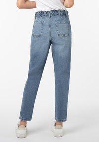 Hellblaue Jeanshose mit gerafftem Bund, zwei hinteren Taschen, geradem Bein Design und subtiler Textur. Weiße Sneakers werden getragen.