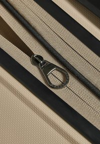 Bolsa con cremallera de tela beige, con tira de cremallera negra y tirador de cremallera metálico, que presenta una superficie texturizada y detalles de diseño elegantes.