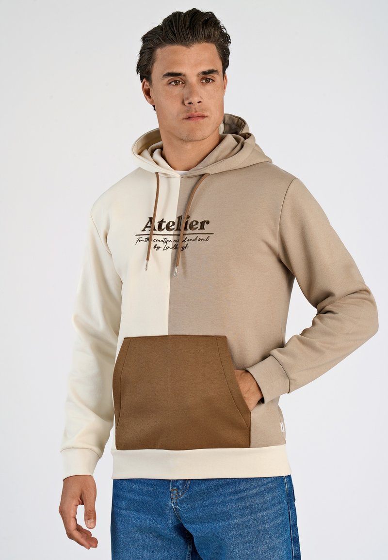 Hoodie met beige en crème kleurblokken, een frontzak en de bedrukte tekst "Atelier" op de borst. Zachte katoenmix stof.