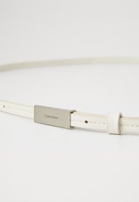 Cintura in pelle bianca Calvin Klein con fibbia in metallo argentato, caratterizzata da incisione del marchio e cuciture sottili lungo la cintura.