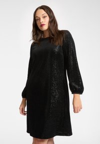 Abito nero con paillettes, taglio morbido, scollo rotondo e maniche a tre quarti. Presenta una superficie strutturata e una delicata brillantezza.