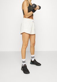 Conjunto deportivo que incluye un sujetador deportivo de camuflaje oscuro, pantalones cortos grises claros con acentos blancos, zapatillas negras y calcetines de rayas hasta el tobillo.