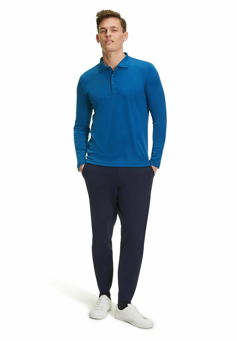 Langärmliges blaues Poloshirt mit geknöpftem Kragen, kombiniert mit marineblauen Hosen und weißen Sneakers; glatte Textur und taillierte Passform.