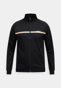 Μαύρο μπουφάν με φερμουάρ από απαλό ύφασμα. Διαθέτει οριζόντια ρίγα σε λευκό και χρυσό χρώμα στο στήθος με το λογότυπο "BOSS" και μπροστινές τσέπες.