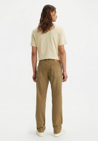 Beige t-shirt en kaki rechte broek, gemaakt van katoen, met twee achterzakken met een leren patch, gedragen met witte sneakers.
