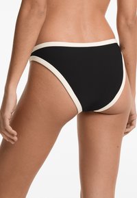 Svart bikini-bottom med en kontrasterande vit kant. Har en klassisk skärning och en slät yta, vilket framhäver en minimalistisk design och rena linjer.