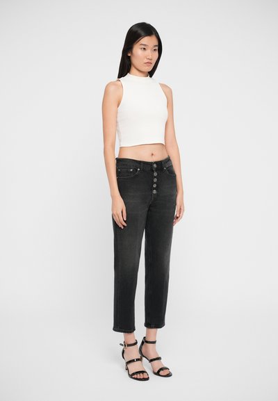 Vaqueros negros de cintura alta con cierre de botones y bolsillos laterales, combinados con una blusa blanca sin mangas ajustada y tacones negros de pulsera en el tobillo.