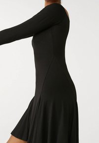 Musta pitkähihainen mekko, jossa on istuva yläosa ja liehuva hame, valmistettu pehmeästä kankaasta, jolla on sileä rakenne, ja siinä on sivuleikkaus.