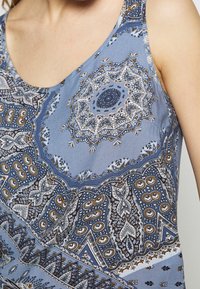 Blå linne med paisleymönster som har intrikata mönster i vitt och brunt. Tillverkat av ett lätt tyg med en slät textur.