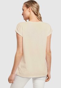 Beige t-shirt lavet af blødt stof, med korte opsmøgssleeves og en rund halsudskæring, med en afslappet pasform og ensfarvet bagside.