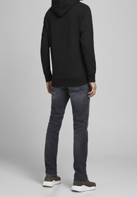 Czarna bluza z kapturem i długimi rękawami, w połączeniu z ciemnoszarymi jeansami. Obuwie z białą podeszwą i brązową cholewką. Ogólnie gładka faktura.