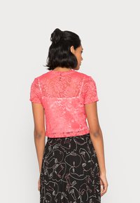 Top em renda rosa de manga curta com um padrão floral, com as costas semi-transparentes, combinado com uma saia preta com rostos desenhados a linha branca.