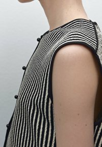 Randig svartvit ärmlös topp med en strukturerad yta, prydd med runda svarta knappar på ena sidan och en böjd utskärning.