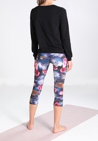 Top negro de manga larga combinado con leggings capri de colores multicolores y estampados que presentan tonos de rosa, azul y gris. Textura de tela suave.