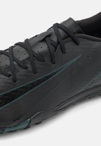 Black athletic shoe with a textured surface, featuring black laces, a subtle blue accent, and a molded sole design for traction.