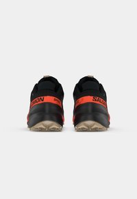 Scarpe da trail running nere e arancioni con suola in gomma testurizzata, dotate di marchio sul tallone e colletto imbottito per il comfort.