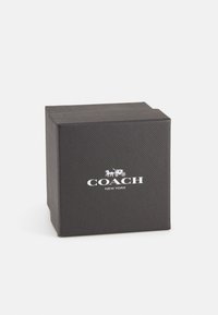 Svart fyrkantig presentask med en textur yta, som har vit "COACH NEW YORK" märkning på framsidan.