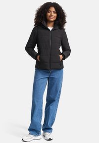 Black padded jacket with a hood, featuring a zip front, side pockets, and elastic cuffs, paired with loose blue jeans and white sneakers.