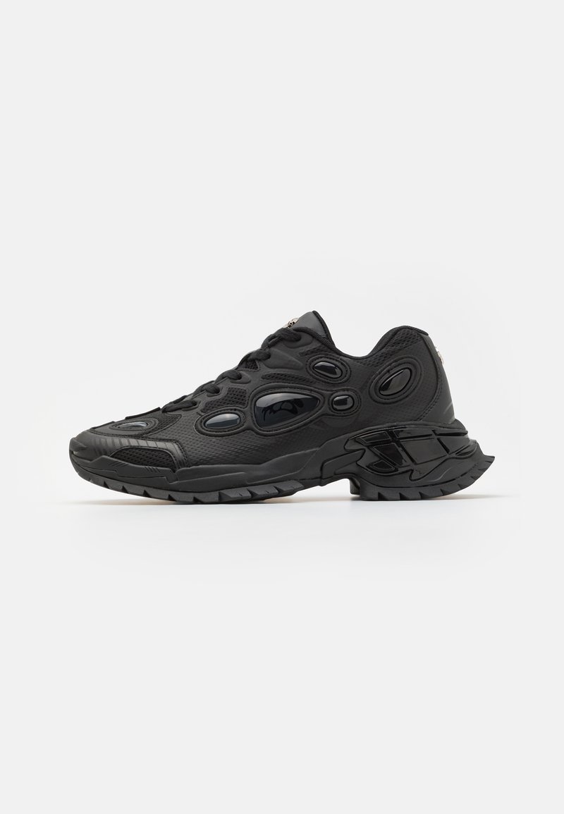 Black athletic shoes with textured synthetic upper, rounded toe, and distinctive oval cutouts. Features a rugged rubber sole for traction.