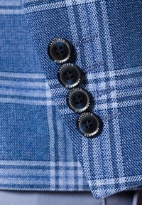 Niebieska marynarka w kratę z rękawem ozdobionym czterema czarnymi guzikami z wygrawerowanym napisem "LANCERTO". Tkanina ma teksturowane sploty i kontrastowe linie.