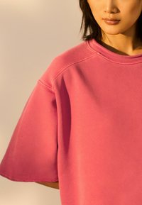 Roze oversized sweatshirt met een ronde hals en korte mouwen, voorzien van een zachte textuur en onafgewerkte zoomdetails.