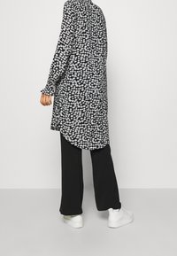 Túnica negra con flores y mangas largas, que presenta flores en blanco y azul claro, combinada con pantalones anchos negros y zapatillas blancas.