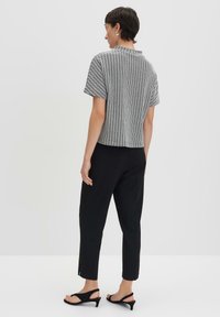 Top a maniche corte a scacchi bianco e nero, vestibilità comoda, abbinato a pantaloni neri a gamba tapered e sandali neri con tacco basso.