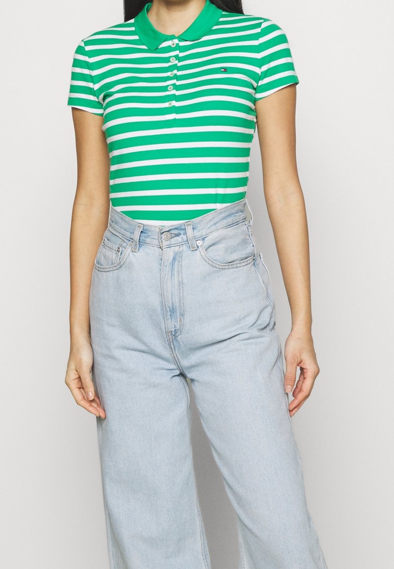 Polo rayé vert et blanc avec col, manches courtes et devant boutonné, associé à un jean taille haute bleu clair.