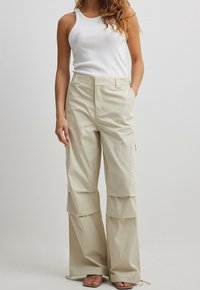 Beige cargo-housut, joissa on löysä leikkaus, kerroksellinen muotoilu, sivutaskut ja nauhakahvat, yhdistetty valkoiseen toppiin.