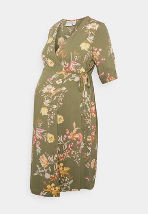 Vestido em tecido floral verde com mangas curtas, apresentando um laço na cintura e uma silhueta fluida. O tecido possui padrões de flores amarelas, rosas e brancas.
