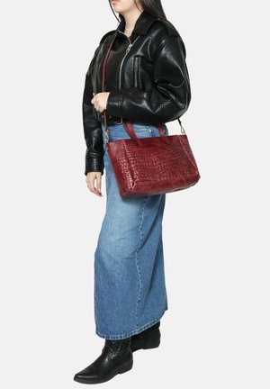 Borsa a mano rossa con impresso coccodrillo, con doppi manici, in tessuto e pelle, forma rettangolare, superficie texture, abbinata a un outfit in denim e pelle.