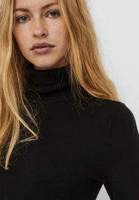 Svart langermet turtleneck-top laget av tettsittende ribbestrikket stoff. Slett tekstur med høy hals og minimale sømmer.